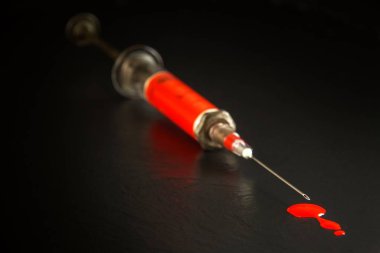 Siyah arka planda şırınga ve kan var. HIV enfeksiyonu riski var. Grip aşısı. Kan testi. Eski şırınga