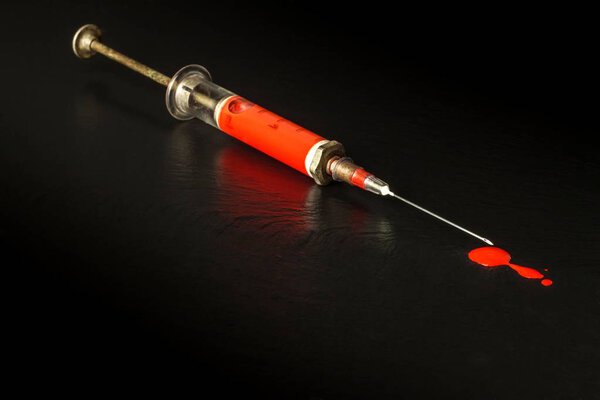 Syringe and blood on black background. Risk of HIV infection. Flu vaccination. Blood test. Old syringe