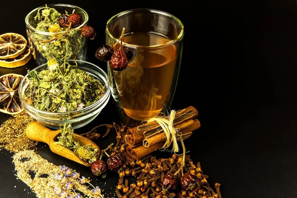 Cup of herbal tea. Various herbal tea ingredients in glass jars over black background. Traditional medicine against flu and cold.