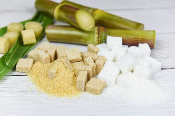 Beyaz ve kahverengi şeker küpleri ve tahta masanın üzerinde şeker kamışı — Stok fotoğraf