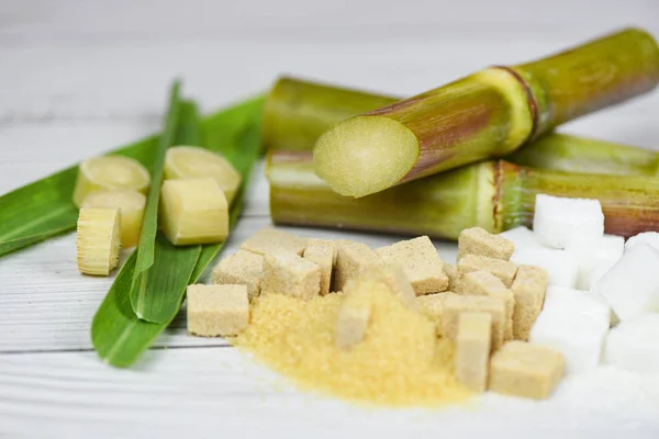 Kostki cukru białego i brązowego oraz trzcina cukrowa na drewnianym stole — Zdjęcie stockowe