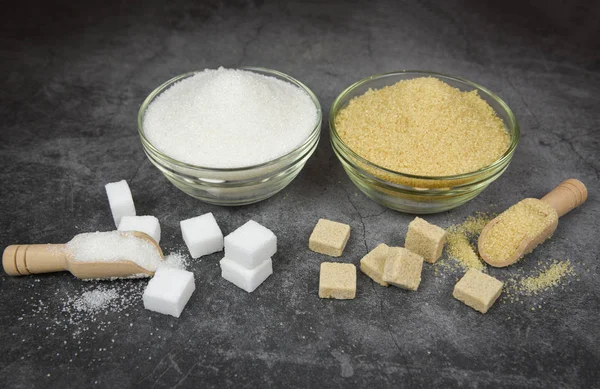 Cubos de azúcar blanco y moreno y un montón de azúcar en un tazón y madera — Foto de Stock