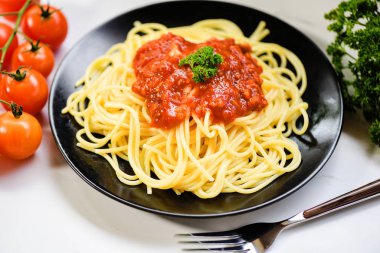 İtalyan spagetti makarnası, siyah tabakta domates ve babayla servis edilir.