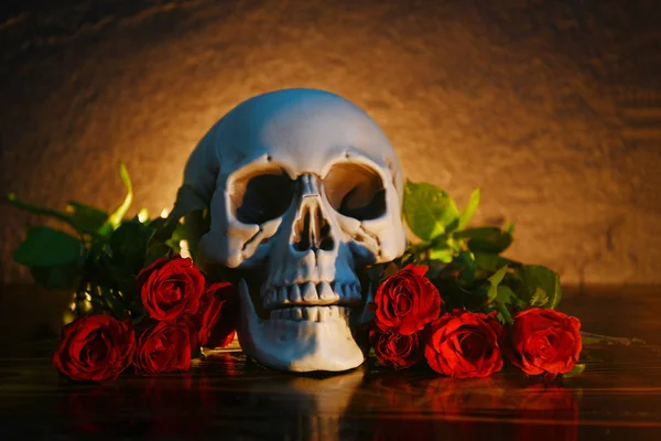 Red roses flower bouquet on rustic wood with skull and candlelig