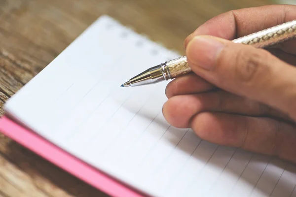Een pen vasthouden op schetsboek of notitieboekje blanco pagina 's op rustiek w — Stockfoto