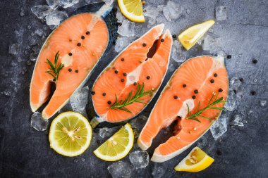 Fresh salmon steak with herbs and spices lemon rosemary on black plate background / Raw salmon fish fillet and ice for cooked steak seafood , top view  