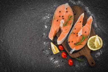 Fresh salmon steak with herbs and spices lemon rosemary tomato on wooden cutting board background / Raw salmon fish fillet and ice for cooked steak seafood , top view  