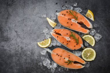 Fresh salmon steak with herbs and spices lemon rosemary on black plate background / Raw salmon fish fillet and ice for cooked steak seafood , top view