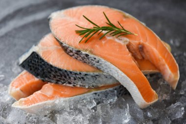Fresh raw salmon steak with herbs rosemary on black plate background / Close up of raw salmon fish fillet and ice
