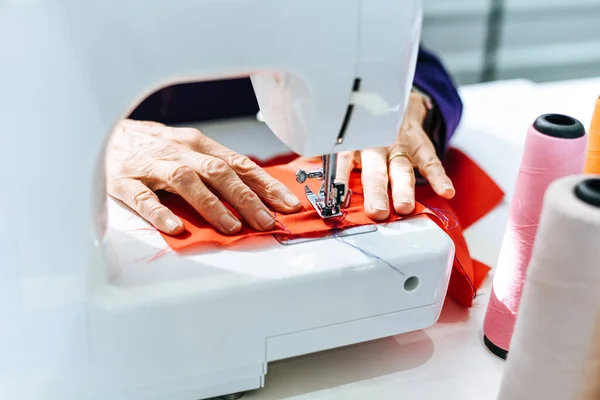 Senior woman tailor working at the sewing factory / Seamstress doing sewing machine sew fabric in the showroom fashion clothes and Sewing thread