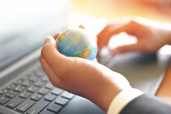 Business man holding earth globe model in hand and use a laptop / Business technology global and around the world concept