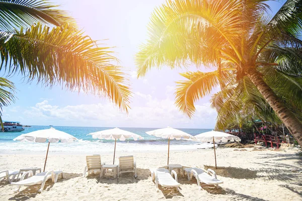 Tropical Holiday coconut leaf palm tree on the beach with sun light on blue sky sea and ocean background / Summer vacation nature travel beautiful summer landscape with chair beach umbrella on sand