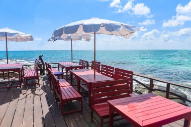 Teras manzaralı deniz, ahşap masa ve sahil manzaralı sandalyeler şemsiyeli güneş ışığı, ahşap balkon manzaralı tatil köyündeki deniz manzaralı cennet gibi deniz manzaralı restoran.