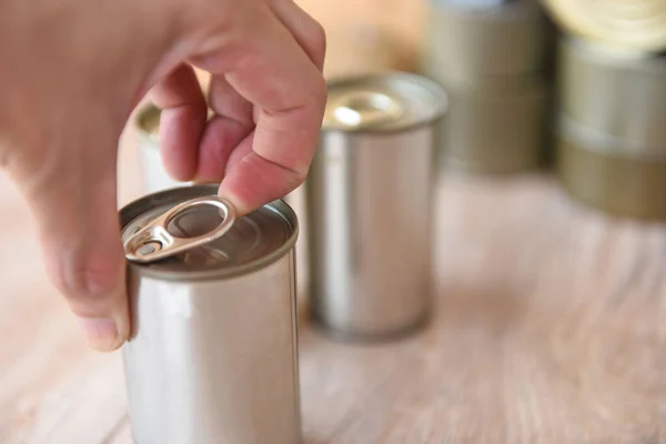 Hand open canned food in metal can on wooden background / Close up canned goods non perishable food storage goods in kitchen home