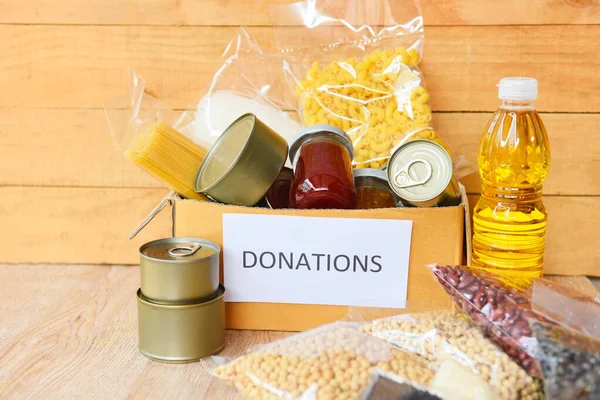 Donations box with canned food on wooden table background / pasta canned goods and dry food non perishable with cooking oil rice noodles spaghetti macaroni donations food concept