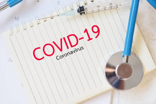 COVID-19 coronavirus concept with syringe injection medication drug and stethoscope on paper notebook / Coronavirus spread influenza medical crisis pandemic public health risk prevention