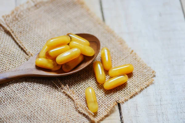 Yellow capsule medicine or supplementary food from nature for health / Royal jelly capsules in wooden spoon and sack background