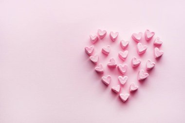 Pink heart-shaped marshmallows stacked on a pink background with