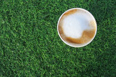 Yeşil çimlerin üzerinde bir fincan kağıt kahve. Yaz atıştırmalığı konsepti