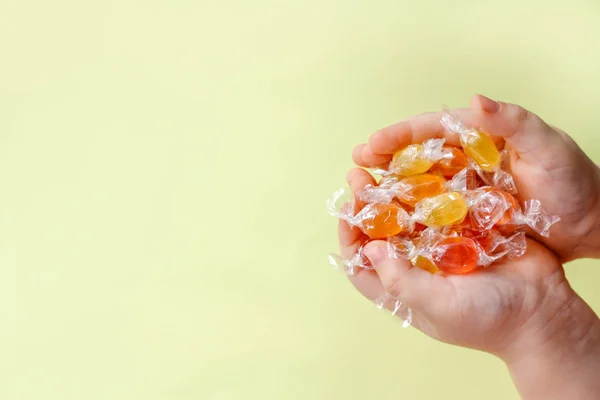 Açık sarı arka planda bir çocuğun ellerinde çok renkli karamel şekerler. Çocuklar için şeker ve ödül kavramı