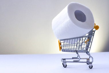 Beyaz arka planda alışveriş arabası olan bir rulo beyaz tuvalet kağıdı. İnsanlar gelecek için satın alıyor. Tüketicilerin koronavirüs paniğinin sembolü olarak alışveriş arabasındaki tuvalet kağıdı rulosu..