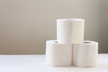 Açık gri arka planda üç rulo beyaz tuvalet kağıdı. İnsanlar gelecek için satın alır.