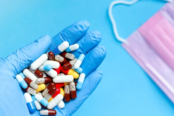 Çok renkli haplar ve pembe bir maske. Farklı boyut ve amaçlara sahip tabletler, küçük ve büyük. Doktorun elleri mavi eldivenli ve çok renkli haplarla. Sağlık hizmeti tıbbi konsepti.