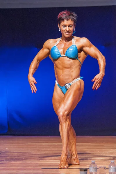 Female bodybuilder flexes her muscles presenting her physique in — Stock Photo, Image