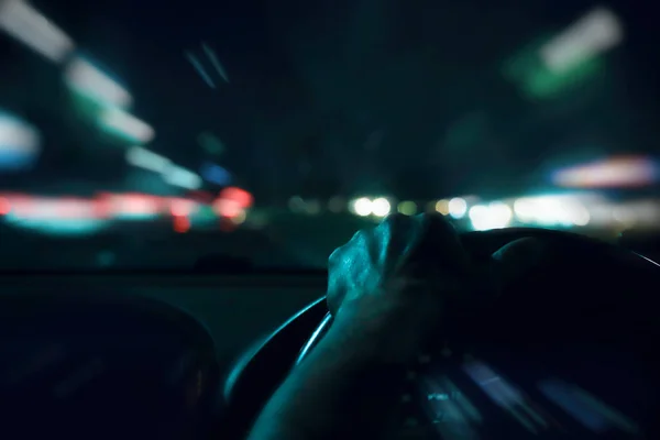 Hombre manos conductor en el volante de un coche moderno con tablero de instrumentos del coche y fondo de la ciudad de la noche. Atasco de tráfico en hora punta en la ciudad. Transporte, Vacaciones, Viajes y Concepto de Automóvil . — Foto de Stock