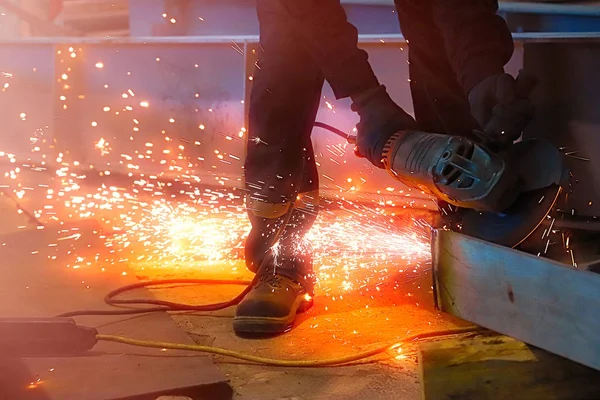 Professional worker cuts metal by angle grinder machine. Fountain of sparks. Fire safety at construction site. Danger and hard work.