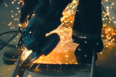 Profesyonel işçiler metali açı öğütücü makinesiyle keser. Kıvılcımlar pınarı. İnşaat alanında yangın güvenliği. Tehlike ve sıkı çalışma.