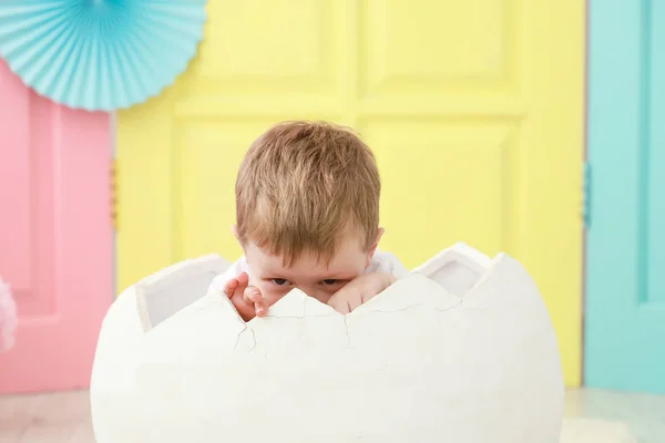 Küçük bir çocuk, beyaz bir yumurtanın içinde oturuyor. Yeni doğan portresi ya da aile konsepti için renkli bir arka plan ile kuluçkaya yatmış.. — Stok fotoğraf