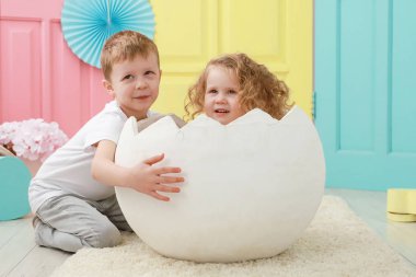 Güzel sarışın kıvırcık kız beyaz bir yumurta ve sarı, pembe ve mavi arka planda beyaz tişörtlü sevimli sarışın erkek portresi içinde oturuyor. Çocuk cinsiyet ilişkileri kavramı.