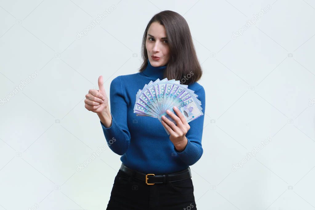 Slender young woman with tenge money, tumb up. White background.