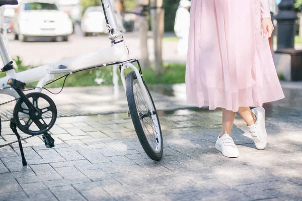 Joven mujer de pie junto a una bicicleta blanca en el parque —  Fotos de Stock