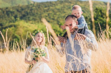 Sıcak ve güneşli yaz gününde buğday tarlasında birlikte yürüyen çocuklu mutlu bir aile. Yumuşak odaklama.