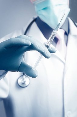 Gazlı bez maskeli bir doktor ve elinde mavi kauçuk eldiveninde şırınga tutan bir doktor. Sağlık ve aşı kavramı