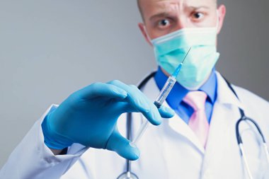 Gazlı bez maskeli ve elinde mavi kauçuk eldiveninde şırınga tutan korkmuş genç bir doktor. Stajyer eğitim konsepti