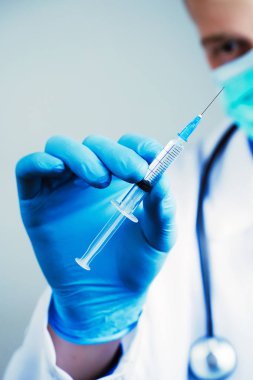 Mavi lateks eldivenli ve şeffaf şırıngalı tıbbi gazlı bez maskeli doktorun elini kapat. Sağlık ve aşı kavramı