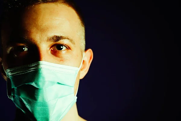 Caucasian man portrait in a medical gauze mask on dark blue background. Virus prevention concept