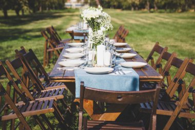 Ahşap masa, yeşil doğanın arka planında servis edilir. Çiçekli vazo.