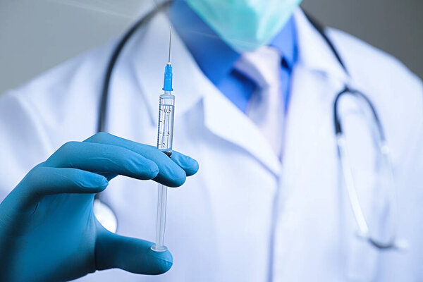 Доктор в марлевой маске и медицинском халате, держащий шприц в голубой латексной перчатке, одетый в руку. Концепция здоровья и вакцинации
