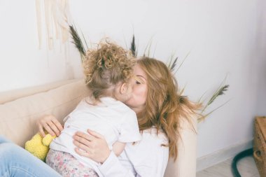 Kızı annesini öpüyor. Genç anne bebeğe sarılıyor..