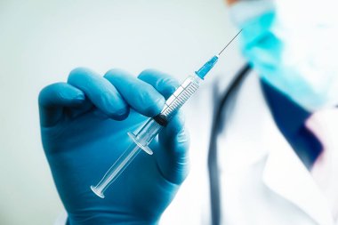 Mavi lateks eldivenli ve şeffaf şırıngalı tıbbi gazlı bez maskeli doktorun elini kapat. Sağlık ve aşı kavramı
