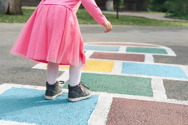 Pembe elbiseli küçük bir kız çocuk parkında seksek oynuyor açık havada çocuk aktiviteleri yapıyor.