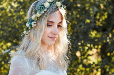 Yaz aylarında açık havada beyaz gelinlik kafasına çiçek buketi ve çelenk ile güzel sarışın genç gelin portresi