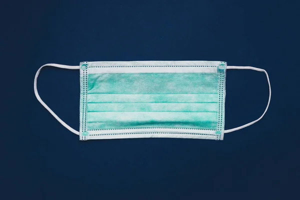 Medical disposable mask on blue paper background, Prevent Covid-19, protection factor for virus. Gloomy toned photo