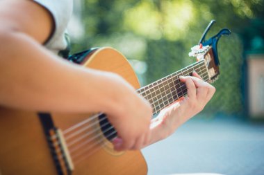 Capo 'nun parktaki gitar boynunu kapat. Parktaki bankta oturan genç adam gitar çalıyor. Genç ve çekici bir adam son bahar tatilinde güneşli günlerde canlı müzik dinlemekten hoşlanıyor. Kullanılan Retro lens.