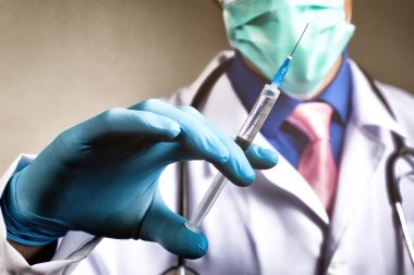 Gazlı bez maskeli bir doktor ve elinde mavi kauçuk eldiveninde şırınga tutan bir doktor. Sağlık ve aşı kavramı