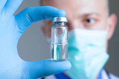 Mavi lateks eldivenli ve cam ampullü tıbbi gazlı maskeli doktorun elini kapat. Sağlık ve aşı kavramı